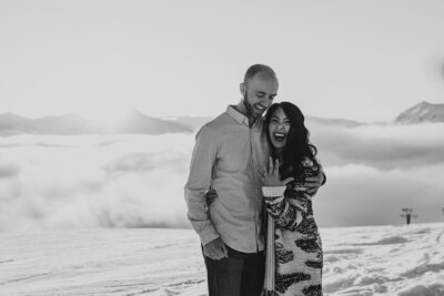 couple excitedly showing off engagement ring against sunny cloudy backdrop at Alyeska