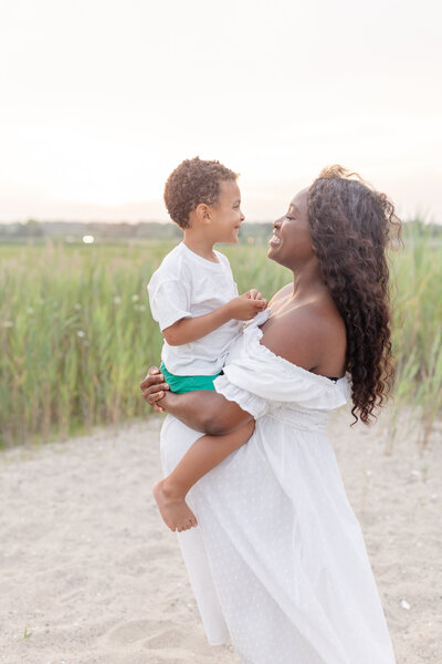 Pregnant mom holding up her child on the beach, gazing at him fondly, capturing a loving and joyful moment between mother and son