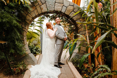 bride and groom standing underneath brick path