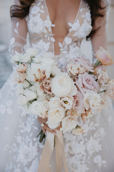 Close-up of a bridal bouquet featuring white and blush flowers held by a bride in a Berta wedding dress.