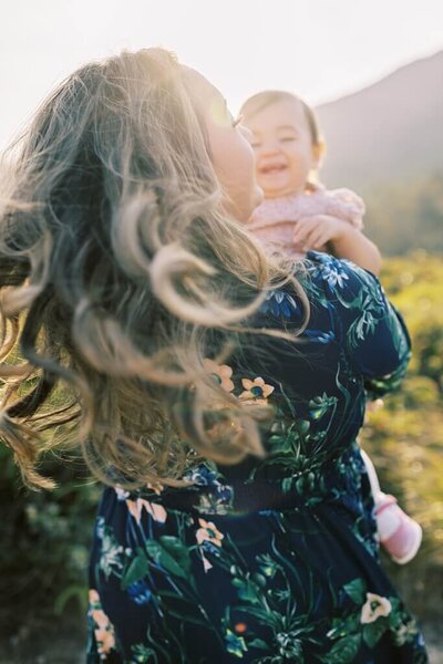 Backshot of a mother in a navy floral dress swaying around with her daughter laughing.