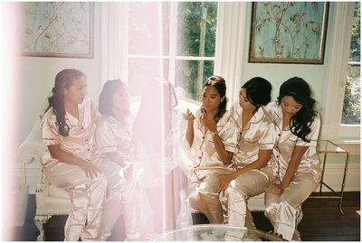 A bride sits on a couch with her bridesmaids in all matching pajamas in getting ready room