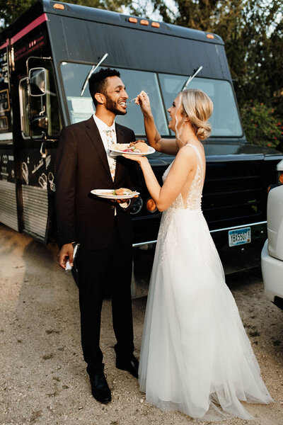 Bride feeds groom in front of a food truck