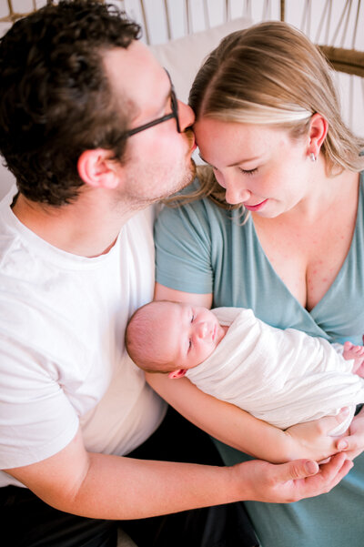 Dad kissing mom on forehead while mom holds newborn baby