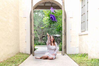 High school senior girl tossing graduation cap in front of Landa Library during senior session in San Antonio, Texas.