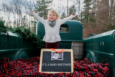 Big sister standing on green truck bed with sign | Maternity Session