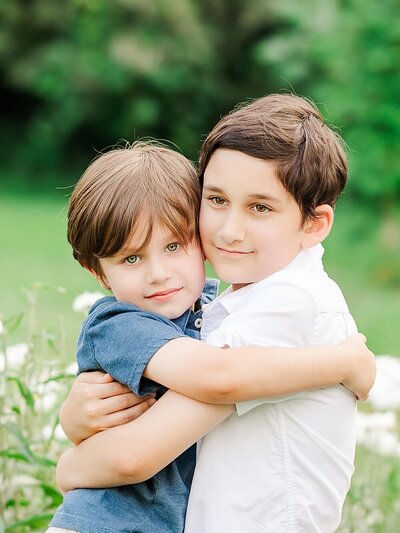 Two brothers hugging each other by white flowers outdoors.
