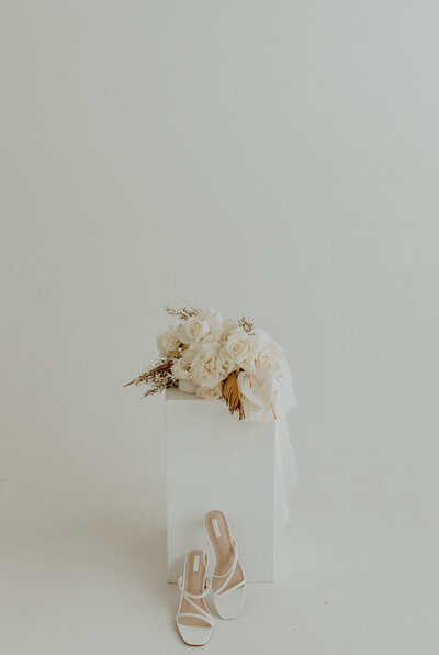 cream bouquet on stand above white heels