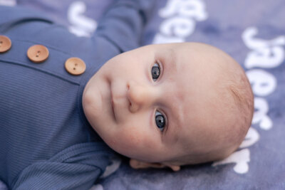 Newborn baby laying on a blanket looking at the camera.