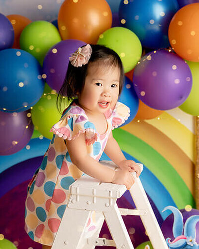 Little girl in a rainbow polka dot dress climbing a ladder to celebrate her birthday.