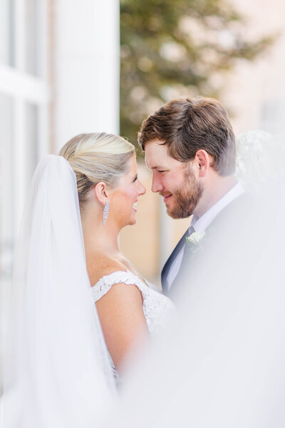 A wedding portrait of the veil swooped towards the camera for beautiful foreground and a bride and groom giggling at each other