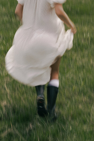 A woman in a white dress running through a green field with flowers and grass, motion blur photo.