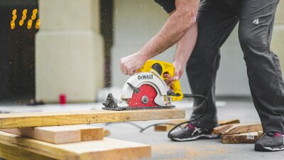A contractor using a circular saw to cut lumber, with wood dust in motion during a home improvement project.