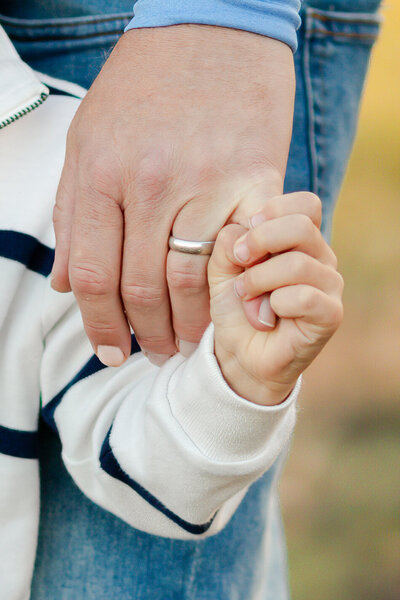 Close-up of a little boy's hand holding his dad's pinkie.