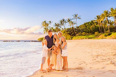 Family embraces on the beach at sunset in Wailea, Maui during their photoshoot with love and water