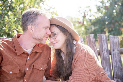 couple sit on swinging bench in an apple orchard and snuggle
