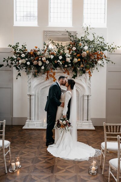 A bride poses and smiles surrounded by lots of greenery and flowers