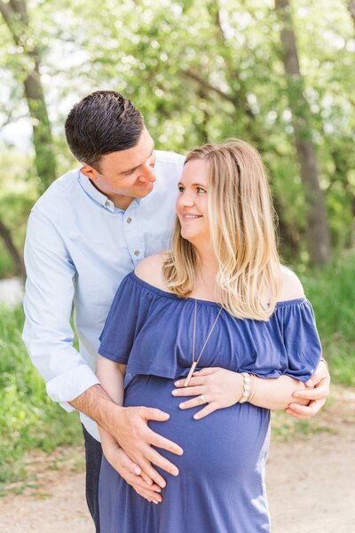 Husband and wife look at each other while holding baby bump longmont co