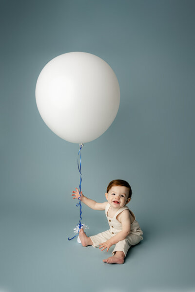 lancaster, sc one year old boy sits with a large white balloon during his studio milestone session