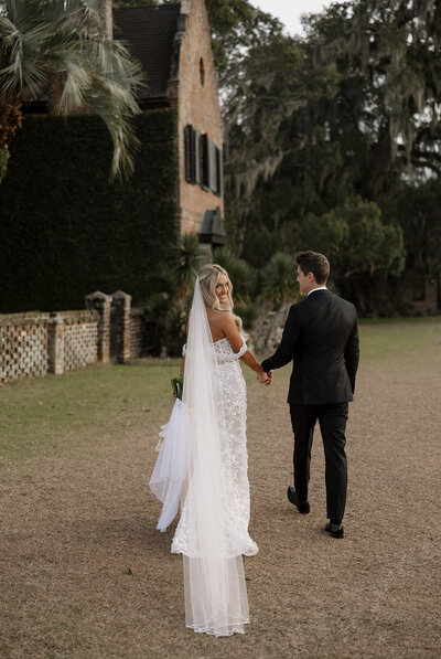bride looking over shoulder while holding grooms hand
