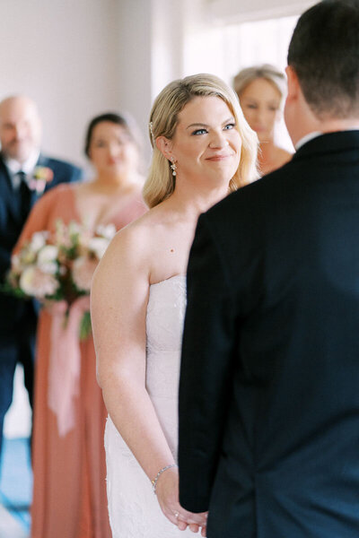 Bride smiling with tears in her eyes as she looks at groom during indoor wedding ceremony in Oakville