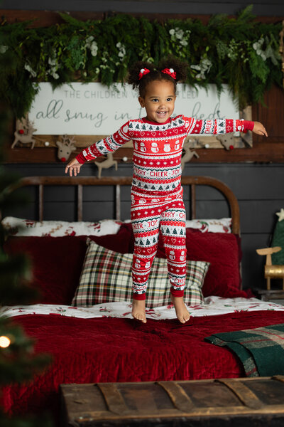 Children in cozy holiday pajamas jumping on a bed and enjoying a fun, festive Christmas photo session in Canton, Georgia.