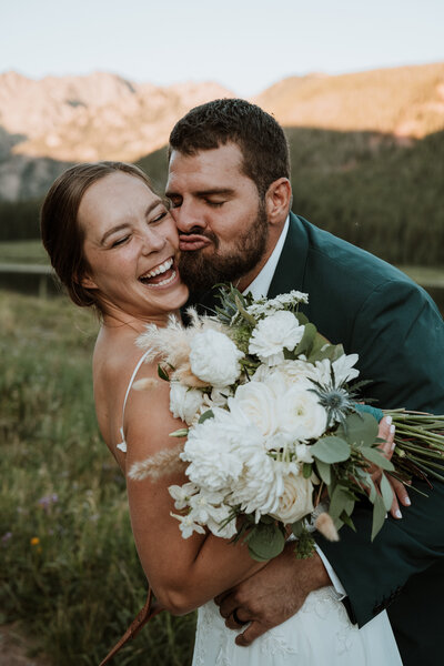 Groom playfully kisses bride holding bouquet at Breckenridge wedding by local elopement photography team.