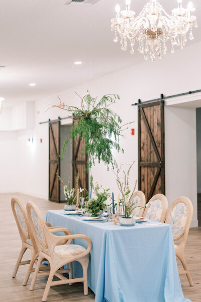 intimate wedding reception space in the Grand Ol Barn in central Florida with a simple table covered in a blue cloth and bright greenery decoration the space