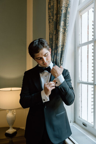 Groom adjusting cufflinks near a window