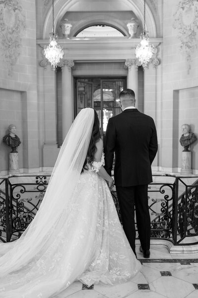A newlywed couple in a tux and gown look over the balcony at the Perry Belmont House in Washington DC