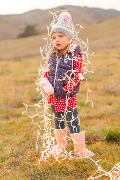 child standing in a field with christmas lights around her