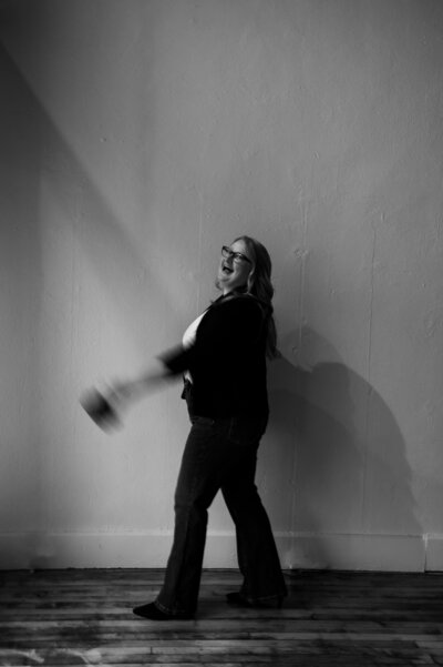 A black and white artistic image of a women walking holding a camera.