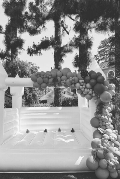 Black and white photo of a bouncy castle with an elegant balloon arch