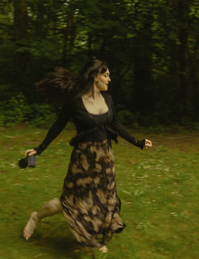 Woman photographer running barefoot through grassy forest clearing with camera