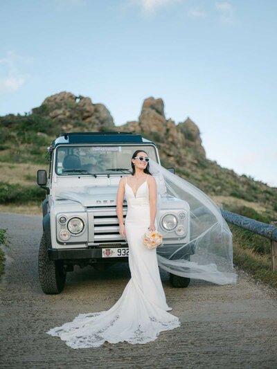 Bride in a chic gown posing with a Land Rover during a luxury destination wedding in St Barth, photographed by Thomas Raboteur