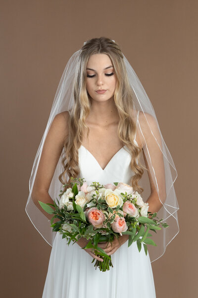 Bride wearing a short two layered veil with ribbon edge and holding a bouquet