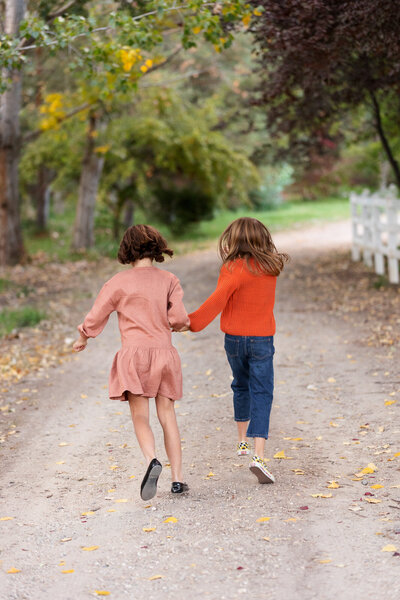 Two sisters skipping down a dirt road during family photography with Tiffany Hix