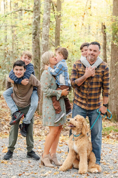 A family of 6 and their dog pose for family photos. The youngest three boys are in the arms of the mom, dad, and oldest son.