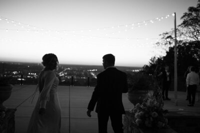 A black and white candid image of a bride and groom walking to the reception