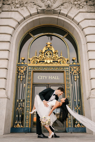 groom dipping bride back while standing on the steps of city hall
