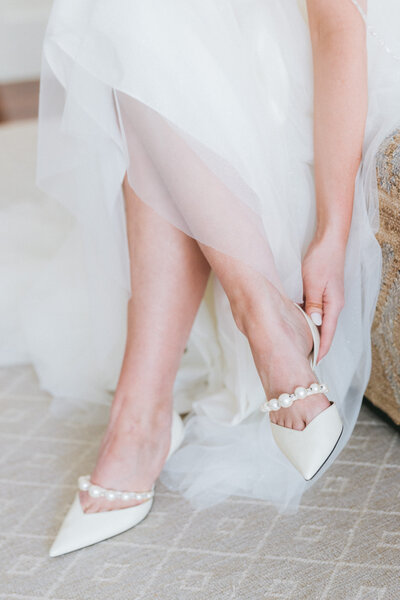 A bride slipping on pearl-embellished wedding heels at her luxury Palmetto Bluff wedding. A refined and elegant bridal detail moment captured beautifully.