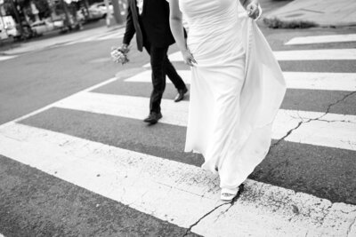 Detail photo of a couple crossing the street in Adams Morgan on their elopement day in DC. The bride is holding her dress as the Groom is walking beside her on the croswalk