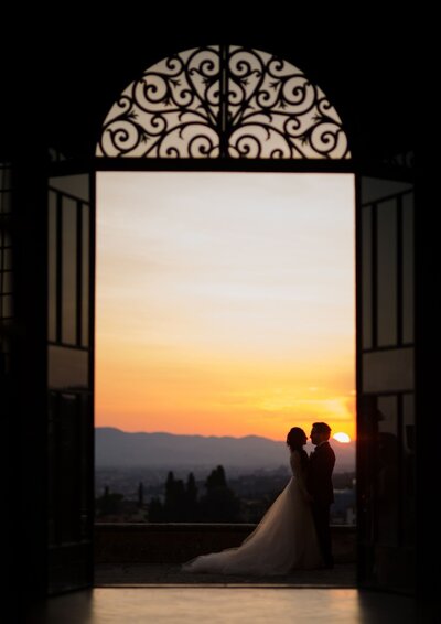 Couples portrait of bride and groom in an ornate doorway with a sunset in the background