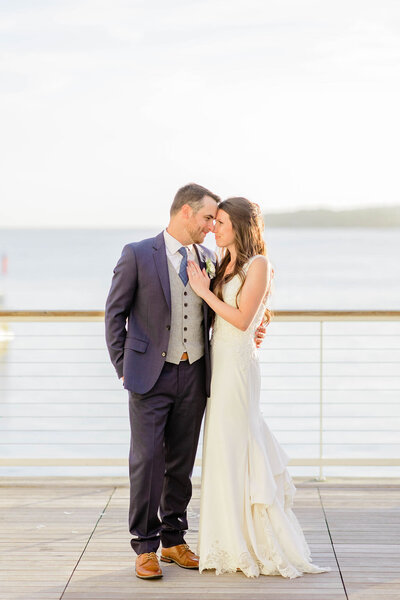 Bride and Groom standing forehead to forehead  at dusk with the water behind them