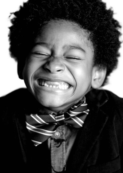 A black and white photo of a young boy wearing a bow tie, smiling and looking directly at the camera.