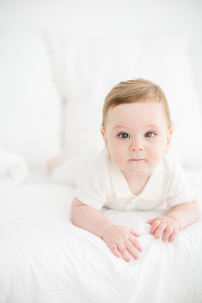 A cozy lifestyle newborn session in the client’s home featuring a swaddled newborn resting peacefully on a bed. Beside the baby, the family dog sits sweetly, watching over its newest family member, creating a heartwarming moment of love and companionship