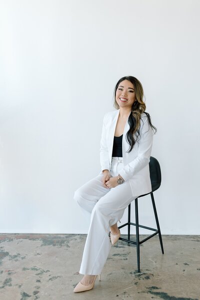 Jessica wearing a white blazer, smiling as she writes in her planner