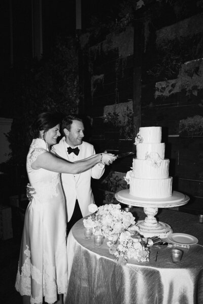 Black and white image of bride and groom cutting cake