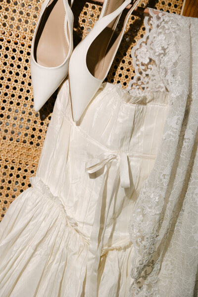 person in white dress and strapy heels standing against a white wall holding a white bouquet