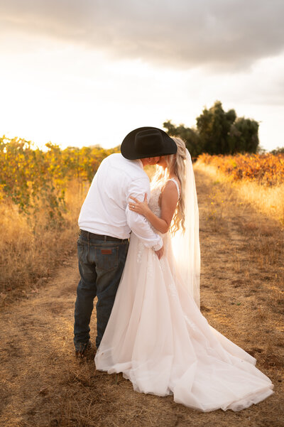 Western bride and groom kiss at sunset. 